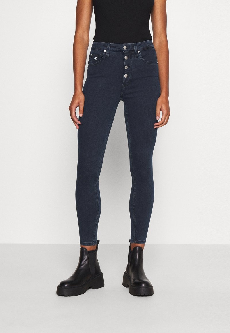 Mörktvättade högmidjade jeans med en figurnära silhuett, femknappsstängning och flera fickor. Matchas med svarta kraftiga ankelstövlar.