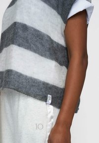 Maglia leggera a righe in grigio e bianco sporco con una vestibilità comoda. Presenta un colletto rotondo e un'etichetta di manutenzione visibile sul lato.