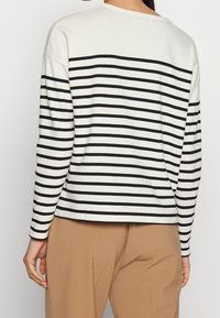 Långärmad topp i svart och vitt randigt, i bomullsmaterial, med rundad halsringning, något lös passform, bakvy som visar det horisontella mönstret.