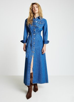 Robe chemise en denim bleu avec manches longues, boutons à l'avant, ceinture à la taille et une fente haute, assortie à des bottes marron en suède montant jusqu'au genou.