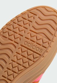 Adidas schoenzool in lichtbruin rubber met een gestructureerd grippatroon met golvende en driehoekige ontwerpen, prominent voorzien van het "adidas"-logo.