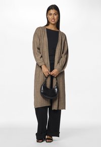 Pikk, ribaga kardigan heledas pruunis, kantud musta sardiini peal. Tumedad lai jalad püksid ja must krokodilli tekstuuriga rahakott täiendavad välimust.