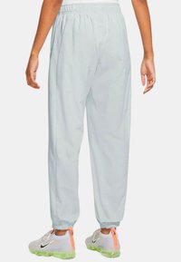 Světle šedé joggingové kalhoty s elastickým pasem, zúženými kotníky a bočními kapsami. Tkanina vypadá hladce a lehce.