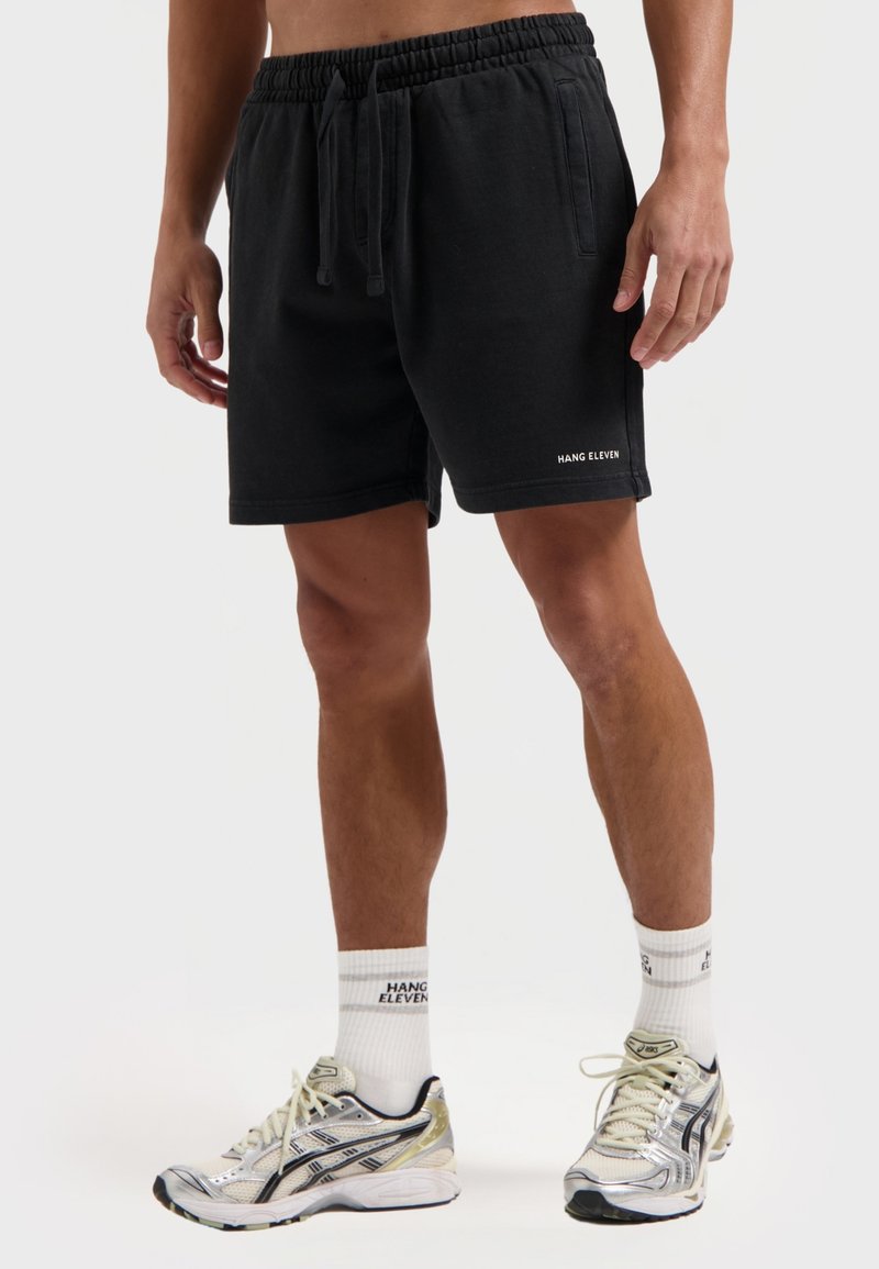 Zwarte katoenen shorts met een elastische tailleband, zijzakken en een klein wit logo op de zoom. Draag ze met sportschoenen en witte sokken.