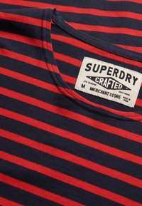 T-shirt à rayures horizontales bleu marine et rouge avec une étiquette blanche Superdry Crafted près de l'encolure, taille moyenne, fabriqué en Inde.