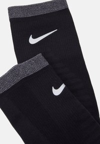 Čierne športové ponožky s textúrovaným telom, šedým rebrovaným manžetou a bielym logom Nike swoosh po boku.