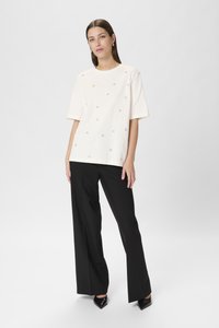Tricou alb din bumbac cu mâneci scurte, decorat cu mici embellishments circulare, asociat cu pantaloni negri largi și pantofi negri ascuțiți.