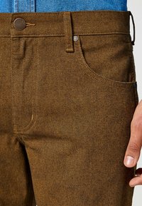 Pantalons bruns texturés à coupe droite, avec un bouton en métal, des poches surpiquées et une ceinture tissée confortable.
