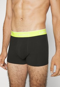 Fekete boxer alsónadrág neon sárga derékkal, amelyen a 'LACOSTE' felirat található. Puha, rugalmas anyagból készült, tetszetős dizájnnal.