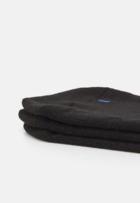 Sorte bomullssokker, brettet i tre lag. Strikket tekstur med subtil ribbing og en liten blå logo detalj på det øverste laget.