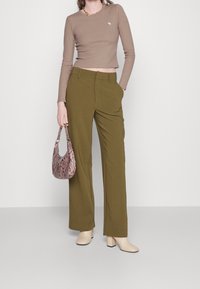 Maglietta aderente a maniche lunghe marrone, pantaloni larghi verde oliva, scarpe con tacco a blocco beige chiaro e una borsa in pelle a forma di serpente rosa.