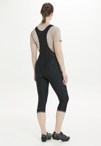 Svarta cykelbyxor med bib, i en åtsittande design, med reflexdetaljer, mesh överdel och knälång längd. Slät textur, elastiskt tyg.