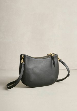 Fekete bőr táska ívelt formával, aranyszínű cipzárral és állítható pánttal. Texturált felületű és minimalista kialakítású.