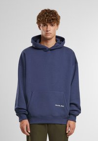 Marineblauwe hoodie van zacht materiaal, met een grote voorzak, een kap met trekkoord en ribgebreide manchetten. Minimalistisch logo detail aan de zoom.