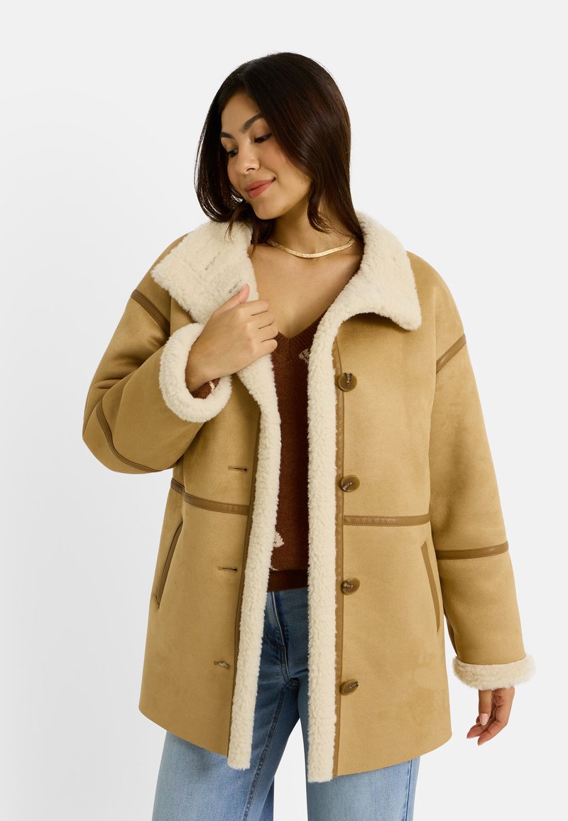 Abrigo marrón de piel sintética con cuello crema, grandes botones y bolsillos laterales, que presenta rayas horizontales en contraste.