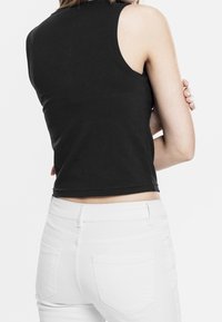 Černý bezrukávový crop top s kulatým výstřihem, hladkou strukturou a přiléhavým střihem, v kombinaci s bílými džíny z denimu s zadními kapsami.