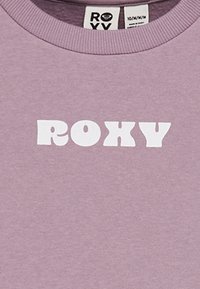 Sudadera lila de textura suave con la atrevida letra blanca "ROXY" en la parte frontal. Cuello redondo con ribete acanalado.