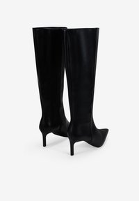 Botas de cuero negro de caña alta, con punta afilada y tacón de aguja delgado, que presentan una textura suave y un diseño elegante y minimalista.