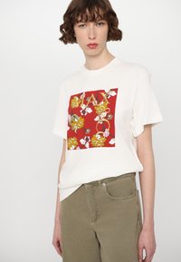 Weißes Baumwoll-T-Shirt mit einem roten Quadrat-Graphic, das mit blumigen Mustern in Gelb und Pink verziert ist, akzentuiert durch das Wort "PLAY". Lässige Passform.
