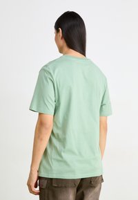 T-shirt κοντομάνικος σε μέντα πράσινο από βαμβάκι με κλασικό λαιμόκοψη, λεία υφή και άνετη εφαρμογή, εμφανίζεται από πίσω.