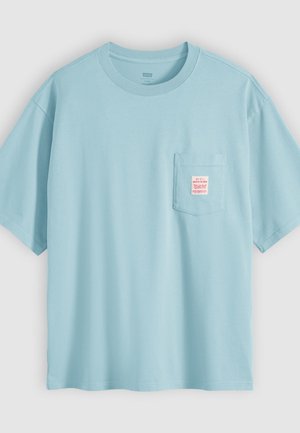 Tricou bleu deschis cu mâneci scurte și buzunar frontal la piept, care are o etichetă mică roz și albă cu text.