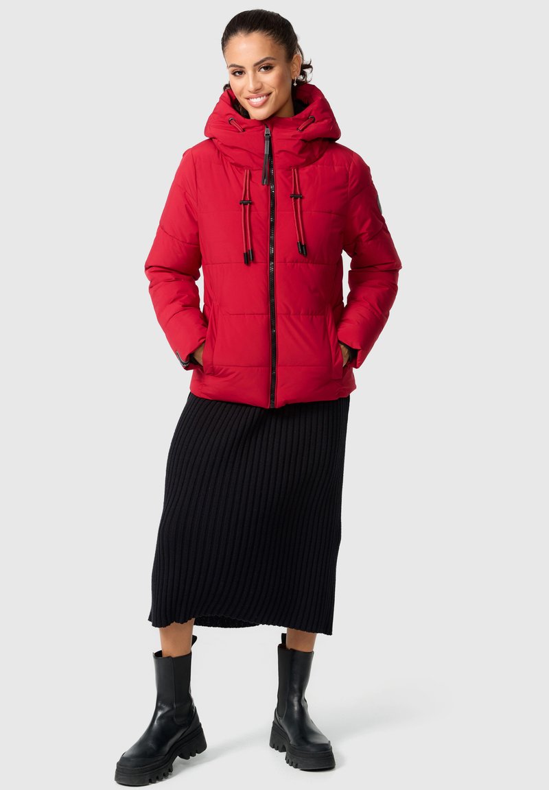 Red padded jacket with a high collar and adjustable drawstrings, paired with a black ribbed skirt and black ankle boots.