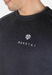 Mørk grå hettegenser laget av myk stoff, med ribbet halslinning og hvit "MOROTAI" logo på brystet.