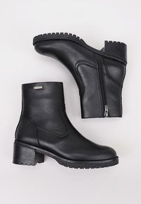 Botas de tobillo de cuero negro con un acabado texturizado, cremallera lateral y un tacón grueso y estriado. Cuenta con una puntera redondeada y un diseño minimalista.