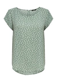 Blouse verte à manches courtes avec des points ovales blancs dispersés et un col rond avec un petit zip au dos.