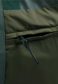 Olivenfarbener Stoff mit einer strukturierten Oberfläche, ausgestattet mit einer Reißverschlusstasche und kontrastierenden dunkelblauen Akzenten entlang der Kanten.