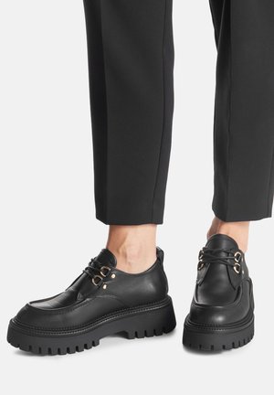 Czarne skórzane buty na sznurowadła z masywną podeszwą z bieżnikiem, wyposażone w metalowe oczka, detale ze szwami i smukły, zaokrąglony kształt.