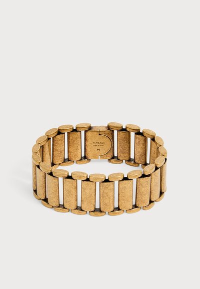 Bracelet en métal ton doré avec des maillons rectangulaires et logo Versace visible sur le fermoir, taille moyenne, sur un fond uni.
