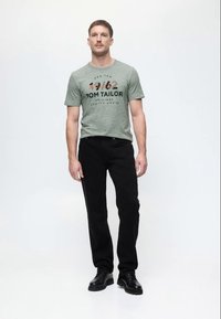 Γκρι κοντομάνικο μπλουζάκι με μαύρο κείμενο, συνδυασμένο με μαύρα τζιν και μαύρα παπούτσια. Η μπλούζα έχει χαλαρή γραμμή και στρογγυλή λαιμόκοψη.