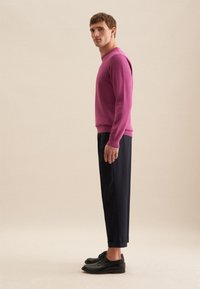 Maglione a maglia fucsia con maniche lunghe abbinato a pantaloni navy su misura e scarpe nere. Tessuto liscio, silhouette aderente e polsini arrotolati.