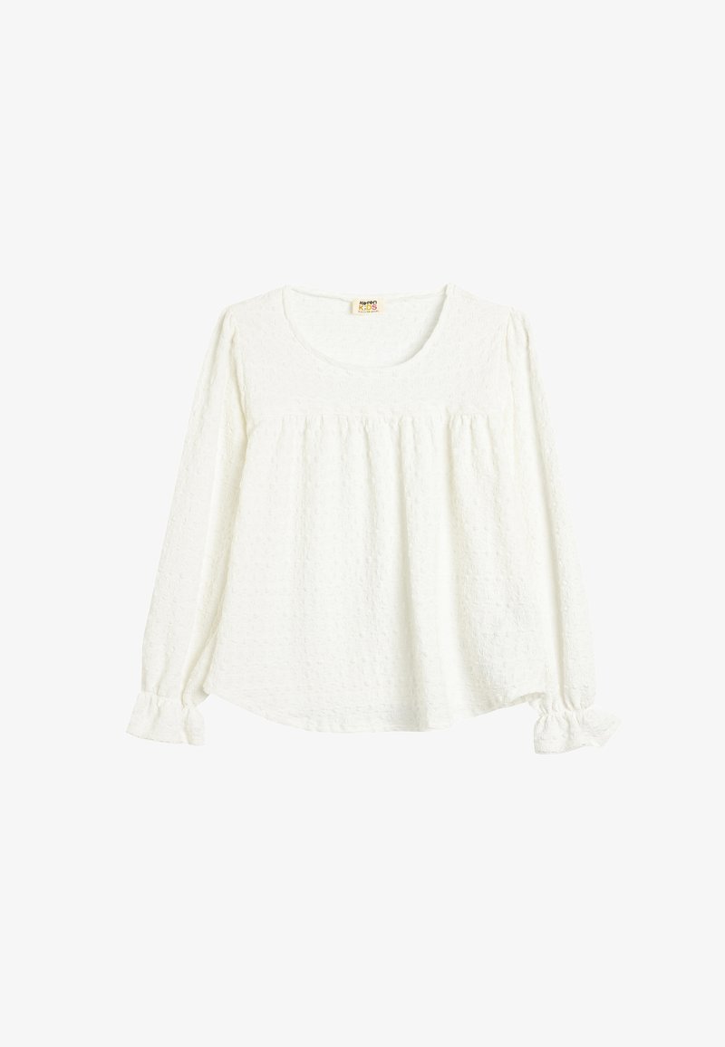Blouse blanche à manches longues en tissu texturé, col rond, devant froncé et poignets élastiqués avec petits volants.