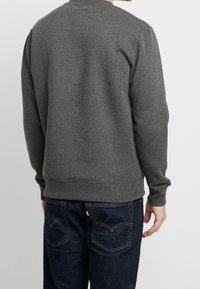 Felpa grigia con scollo rotondo, polsini e orlo a costine, realizzata in una miscela di cotone liscia, abbinata a jeans blu scuro con cuciture sulle tasche posteriori.