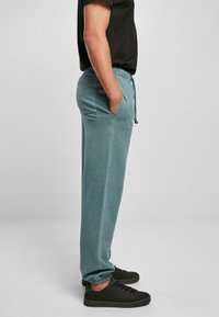Lys teal joggebukser i mykt stoff, med elastisk midje, snøring, sidelommer og ribbede mansjetter. Brukt med svarte joggesko.
