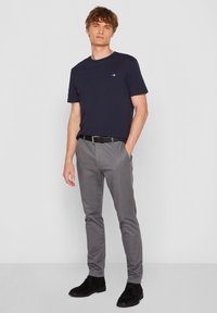 Granatowa koszulka z okrągłym dekoltem zestawiona z jasnoszarymi spodniami o wąskim kroju, podkreślona czarnym paskiem i czarnymi zamszowymi botkami za kostkę.