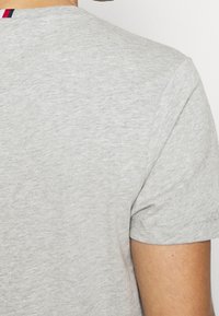 Camiseta gris con escote redondo, mangas cortas y una tela suave y texturizada. La vista trasera muestra una franja de color contrastante en el cuello.