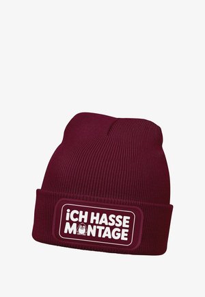 Maroon knitted beanie with a ribbed texture, featuring a white rectangular patch with the text "ICH HASSE MONTAGE" and a small cartoon character.