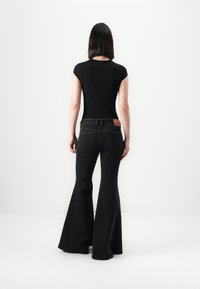 Top aderente nero a maniche corte abbinato a jeans neri a vita alta e a campana. I jeans presentano un design con tasca posteriore e un etichetta con logo.