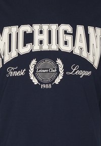 Camiseta azul marino con gran texto blanco que dice "MICHIGAN," con "Finest," "League," y un emblema circular con "Leisure Club" y el año 1988.