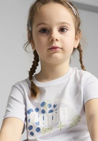 Bílá bavlněná tričko s modrým a zeleným grafickým designem, včetně textu "PUMA", teček a loga. Krátké rukávy s kulatým výstřihem.