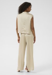 Haut beige sans manches avec un col montant et une texture plissée, assorti à un pantalon à jambe large, le tout en tissu lisse.