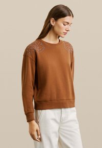 Sudadera marrón con cuello redondo y mangas largas. Presenta un intrincado detalle de cuentas en los hombros. Terminada con un dobladillo y puños de canalé.
