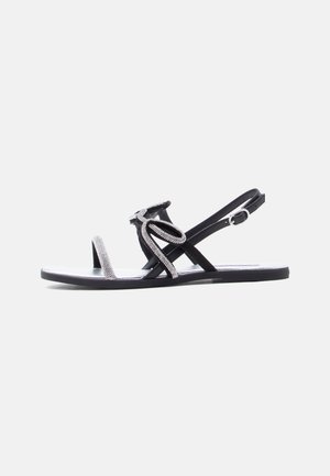 Črni ravni sandal z naramnicami za prste, okrašenimi z okrasnimi kamenčki, in zgornjim dizajnom z zanko, ki ima nastavljiv trak za zaponko okoli gležnja.