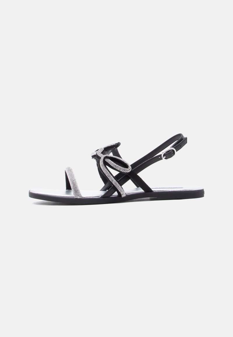 Μαύρο επίπεδο σανδάλι με λουράκι δαχτύλου διακοσμημένο με κρύσταλλα και σχεδιασμό επάνω μέρους με θηλιές, διαθέτοντας ρυθμιζόμενο λουράκι αστραγάλου με αγκράφα.