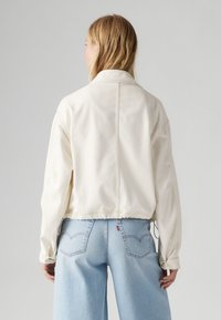 Crème-kleurige cropped jack met een kraag, lange mouwen en een verstelbare zoom. Kenmerkt zich door stikselaccenten en een ontspannen pasvorm.