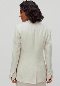 Lichtbeige linnen blazer met een getailleerde pasvorm, lange mouwen, splitmanchetten en een schone achternaad. Gladde textuur, minimalistisch ontwerp.