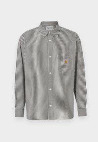 Camisa de manga larga con rayas verticales en blanco y negro y cuello abotonado. Cuenta con un bolsillo en el pecho con un parche de logo beige.